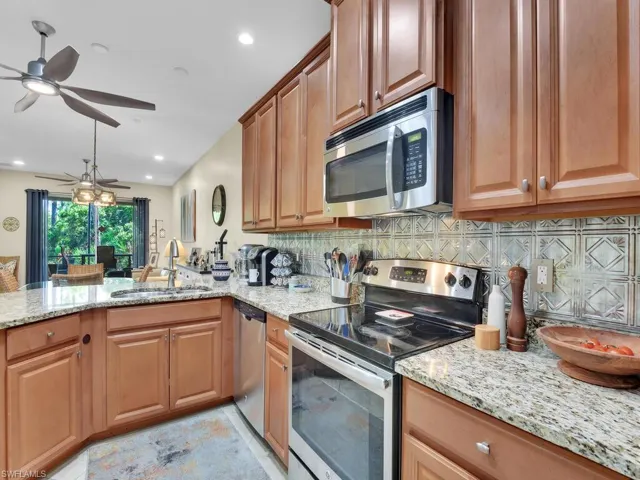 Kitchen with backsplash, stainless steel appliances, light stone counters, sink, and ceiling fan