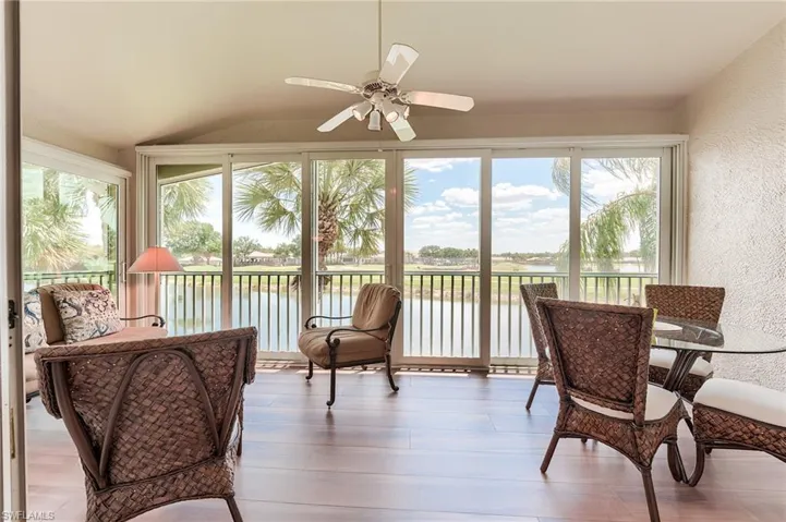 Sunroom featuring vaulted ceiling, a textured wall, a water view, and wood finished floors