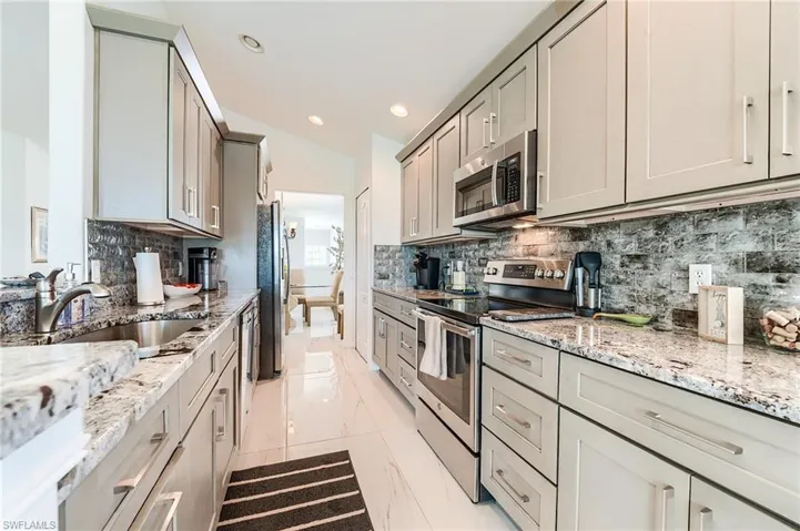 Kitchen featuring light stone counters, a sink, decorative backsplash, gray cabinets, and stainless steel appliances