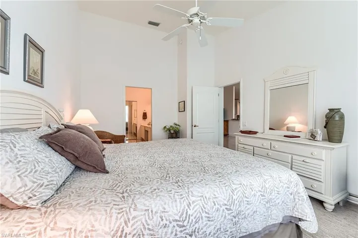 Bedroom featuring visible vents, light colored carpet, ensuite bath, high vaulted ceiling, and ceiling fan