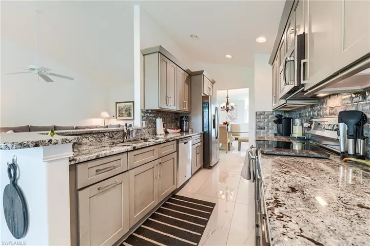 Kitchen featuring stainless steel appliances, a peninsula, a sink, backsplash, and gray cabinetry