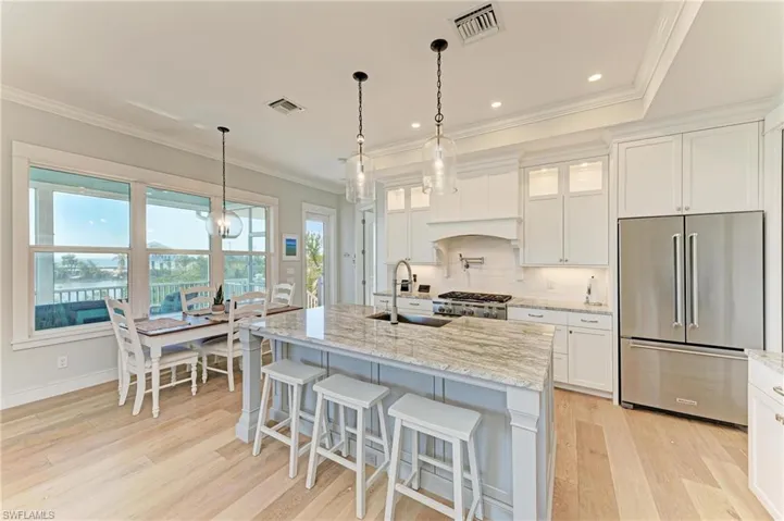 Kitchen featuring light stone counters, high end refrigerator, an island with sink, and white cabinets