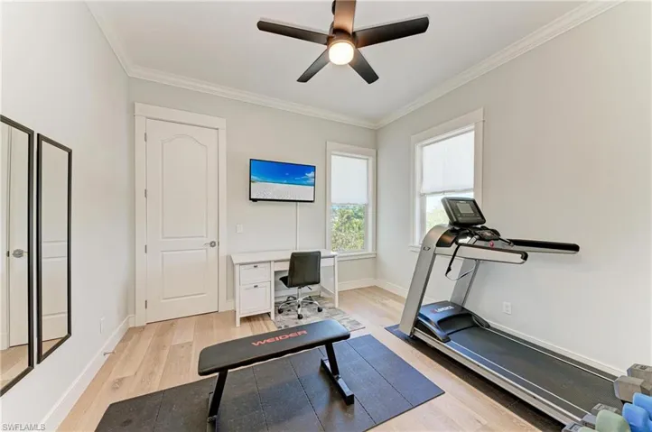 Exercise room with ornamental molding, ceiling fan, and light wood-type flooring