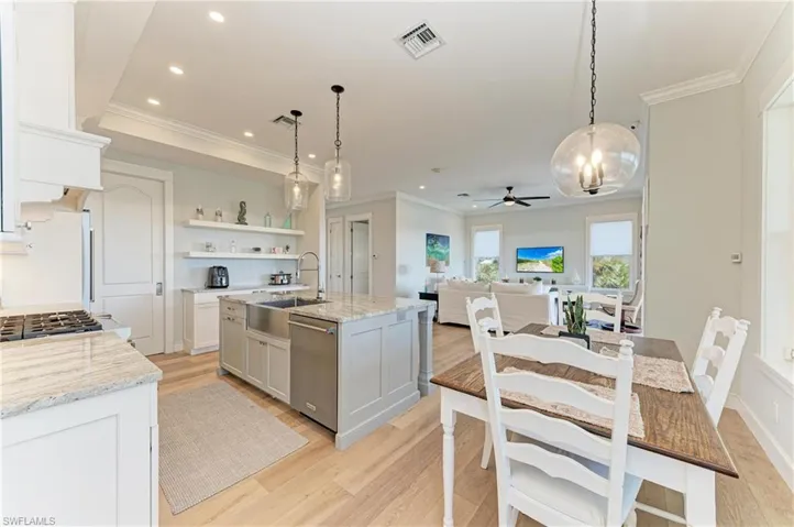 Kitchen featuring white cabinetry, dishwasher, a kitchen island with sink, and hanging light fixtures