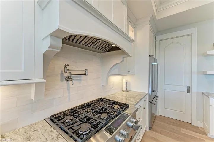 Kitchen featuring light hardwood / wood-style flooring, appliances with stainless steel finishes, backsplash, light stone counters, and white cabinets
