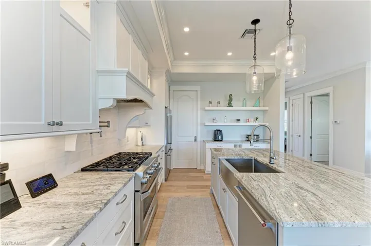 Kitchen with high quality appliances, white cabinetry, hanging light fixtures, light stone countertops, and a center island with sink