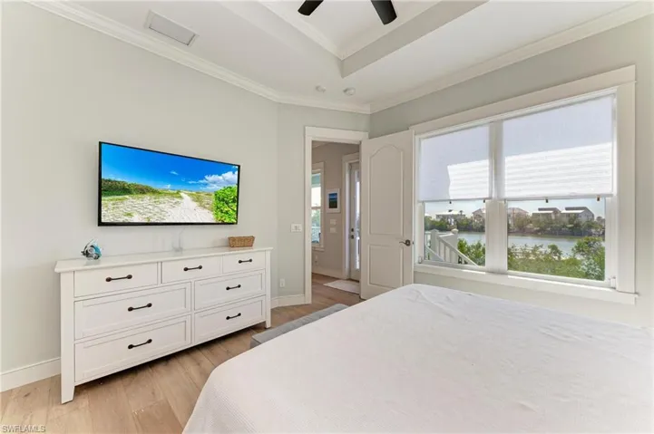 Bedroom featuring a tray ceiling, light hardwood / wood-style flooring, ornamental molding, and ceiling fan