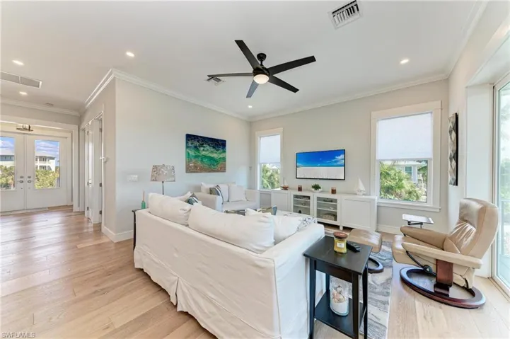 Living room with ornamental molding, french doors, ceiling fan, and light wood-type flooring