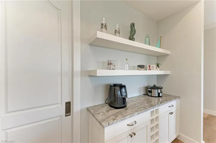 Bar with white cabinetry and light stone counters