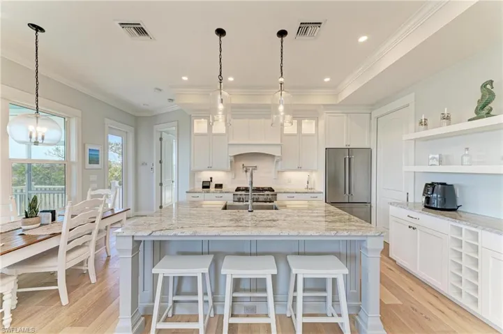 Kitchen featuring white cabinetry, hanging light fixtures, a center island with sink, high quality fridge, and light stone countertops