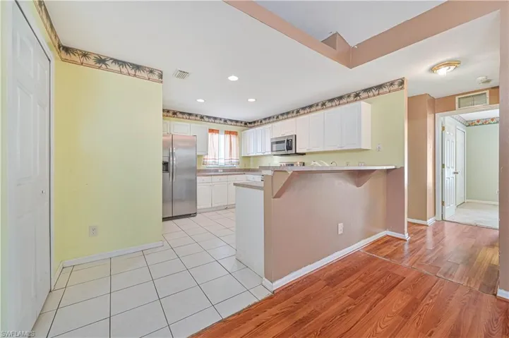 Kitchen featuring light wood-type flooring, stainless steel appliances, a kitchen breakfast bar, and white cabinetry