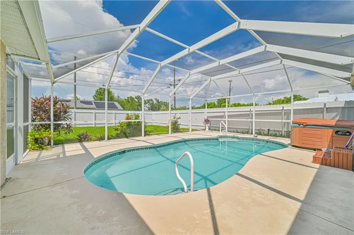 View of pool featuring a hot tub, glass enclosure, and a patio