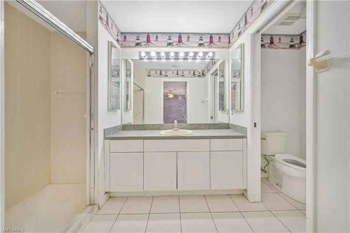 Bathroom featuring tile patterned floors, vanity, walk in shower, and toilet