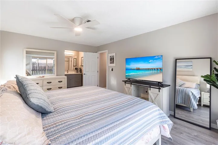 Bedroom featuring a ceiling fan, ensuite bath, light wood-style floors, and large screen T.V.