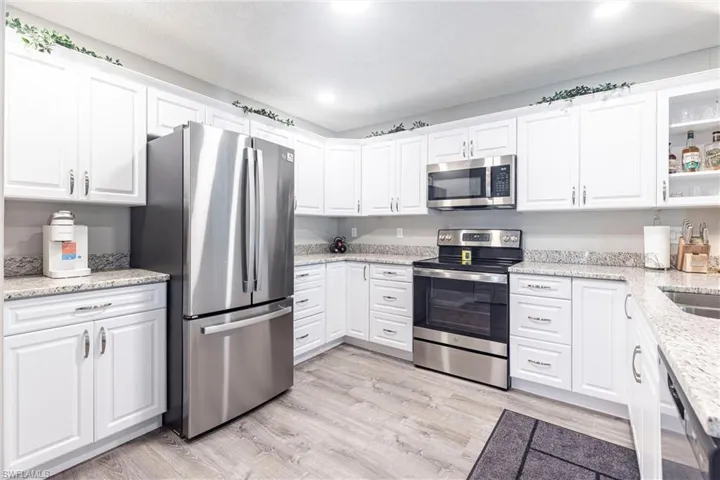 Kitchen with stainless steel appliances, light wood-style floors, white cabinets, glass insert cabinets, and light stone countertops