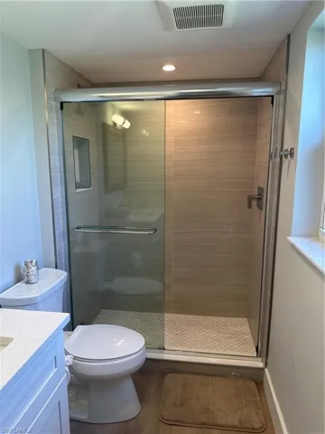 Bathroom with visible vents, toilet, wood finished floors, vanity, and a stall shower