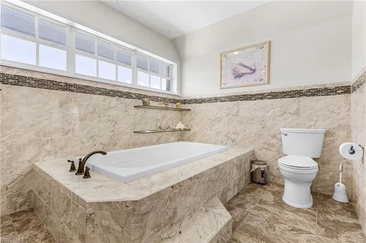 Full bath with a bath, tile walls, and wainscoting