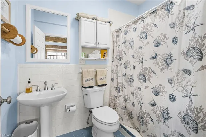 Bathroom with tile walls, tile patterned floors, a shower with curtain, and a wainscoted wall