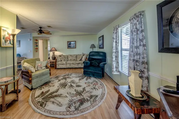 Living area featuring ceiling fan, light wood-style flooring, vaulted ceiling, and crown molding