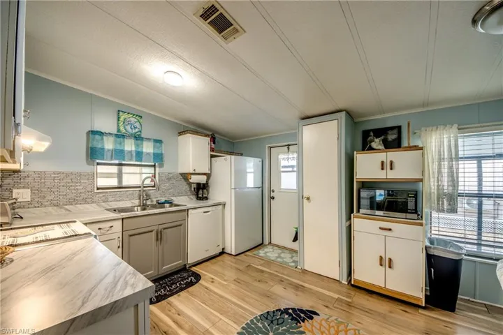 Kitchen featuring tasteful backsplash, light countertops, white dishwasher, light wood-style flooring, and black microwave