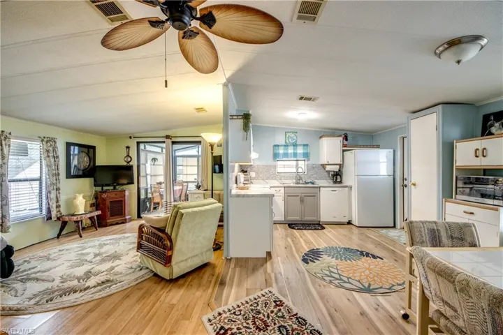 Living area with ornamental molding, healthy amount of natural light, light wood-style floors, ceiling fan, and vaulted ceiling