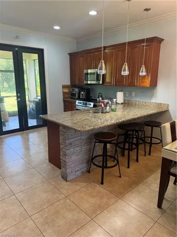 Kitchen featuring a breakfast bar, a peninsula, ornamental molding, pendant lighting, and light tile patterned floors