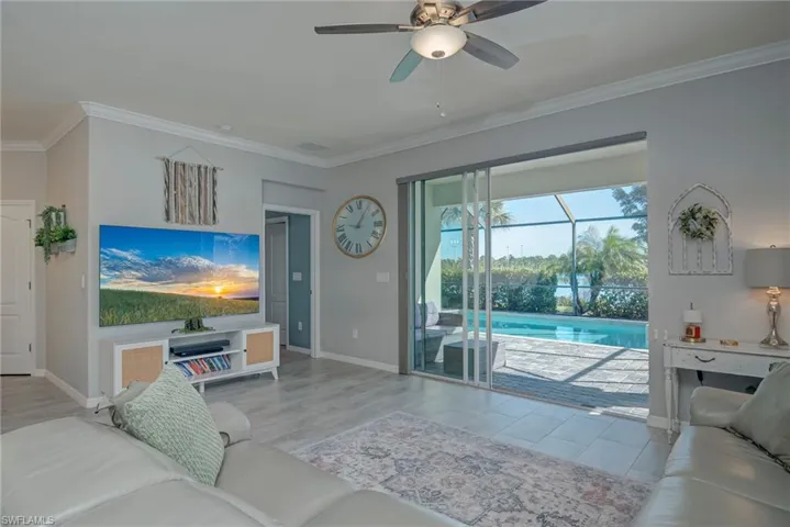 Living area with ornamental molding, a ceiling fan, light wide plank tile floors over looking the pool.