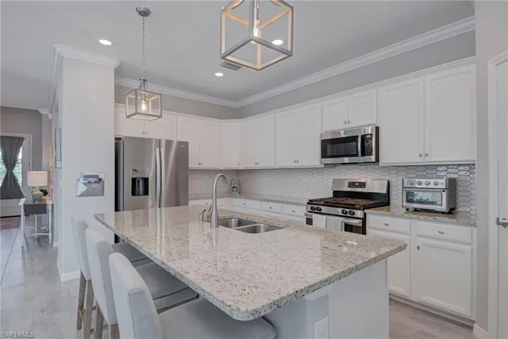 Kitchen featuring appliances with stainless steel finishes, a breakfast bar, light stone counters, white cabinetry, and an island with sink