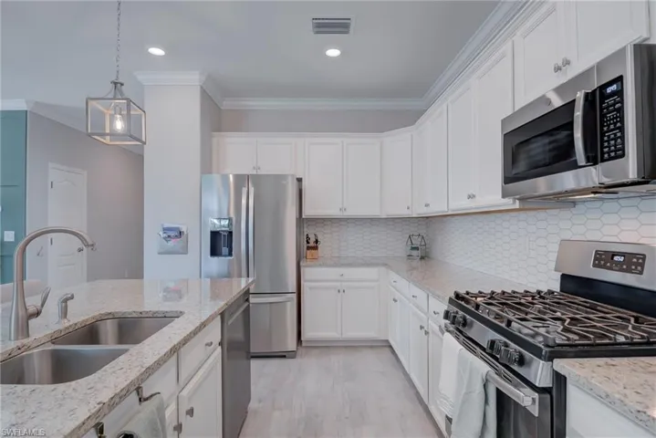 Kitchen featuring stainless steel appliances, ornamental molding, hanging light fixtures, white cabinets, and recessed lighting