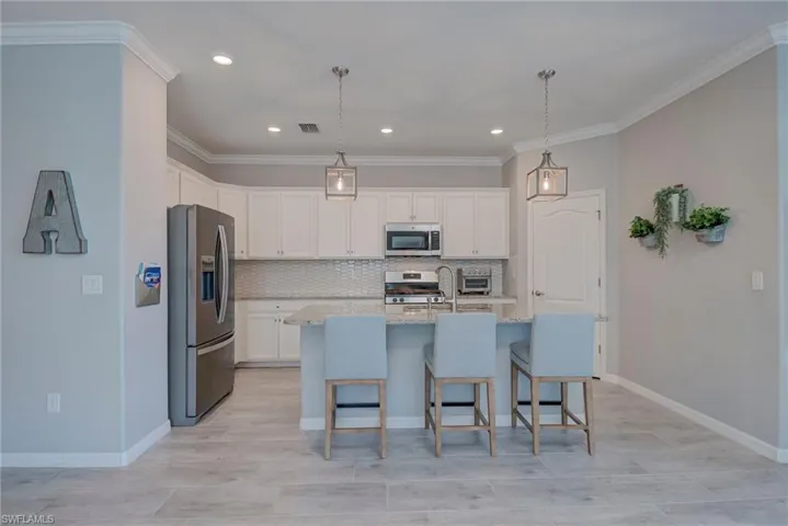 Kitchen with appliances with stainless steel finishes, a breakfast bar area, crown molding, white cabinets, custom backsplash and hanging light fixtures