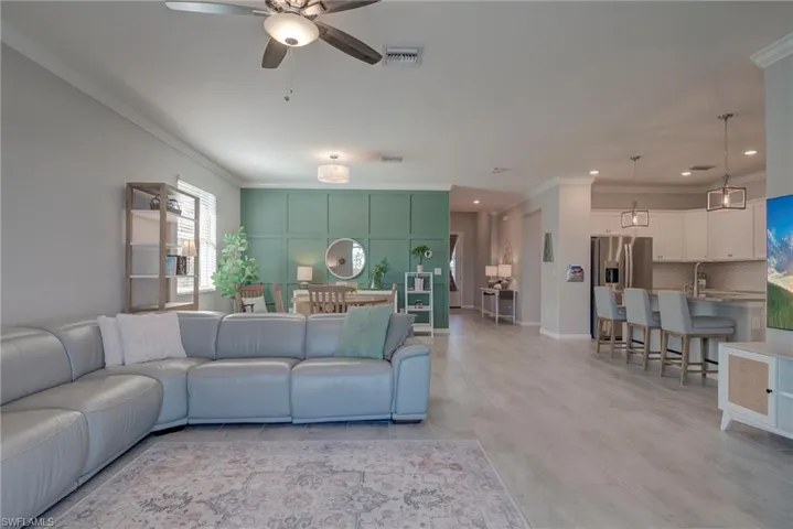 Living room with ornamental molding, ceiling fan, and light wood-style floors