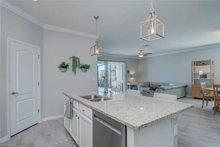 Kitchen with pendant lighting, crown molding, dishwasher, light stone countertops, and ceiling fan