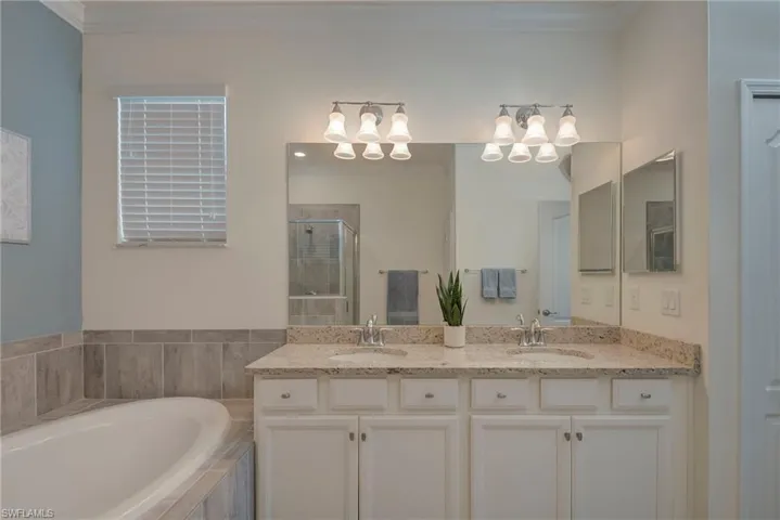 Full bath featuring double vanity, a bath, ornamental molding, and a stall shower