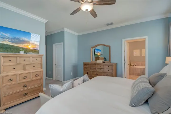 Bedroom featuring light carpet, ornamental molding, ceiling fan, and connected bathroom