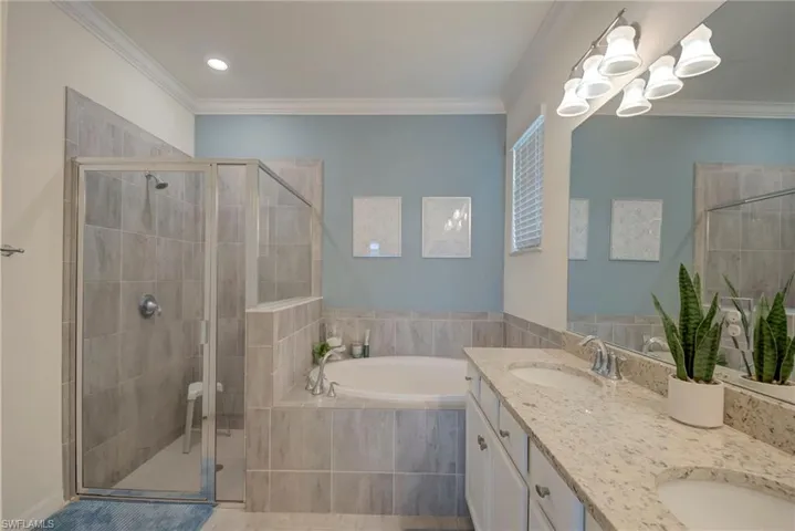 Bathroom with a bath, double vanity, crown molding, a shower stall, and recessed lighting