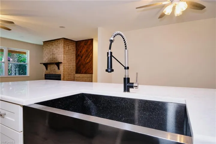 Kitchen view of a ceiling fan, a brick fireplace, light stone countertops, and white cabinets