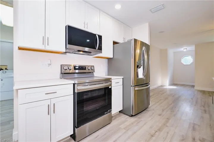 Kitchen with appliances with stainless steel finishes, white cabinetry, light countertops, and washer / clothes dryer