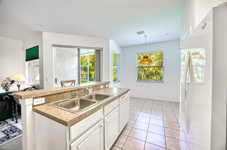 Kitchen with white appliances, hanging light fixtures, light tile patterned floors, an island with sink, and sink