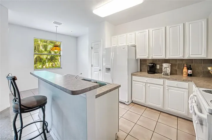 Kitchen featuring white appliances, white cabinetry, pendant lighting, and backsplash