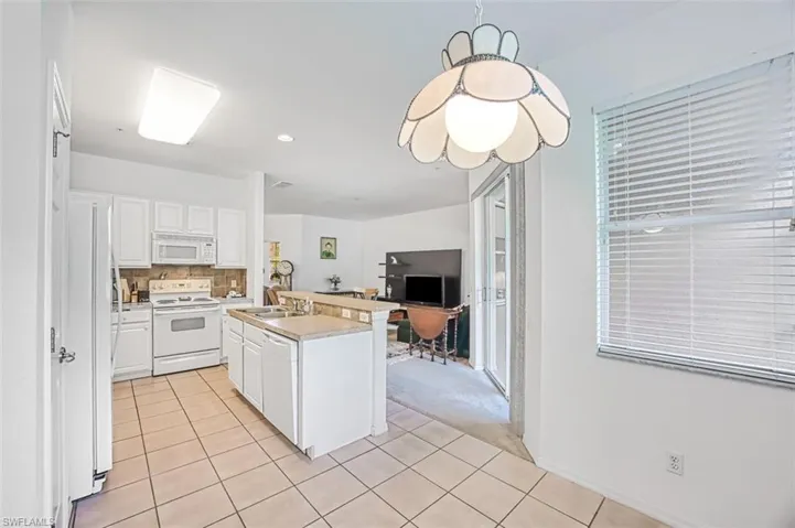 Kitchen featuring tasteful backsplash, white appliances, a center island with sink, light tile patterned floors, and white cabinets