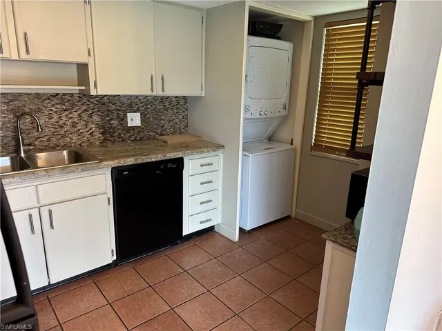 Kitchen with sink, stacked washer / dryer, white cabinetry, black dishwasher, and decorative backsplash