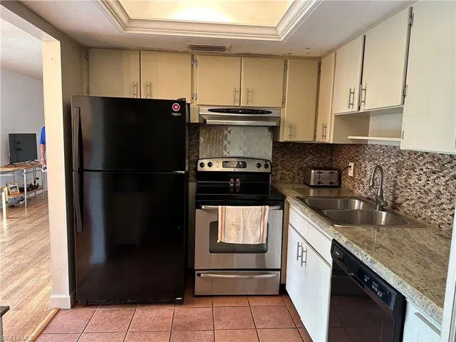 Kitchen featuring light wood-type flooring, black appliances, sink, and a raised ceiling