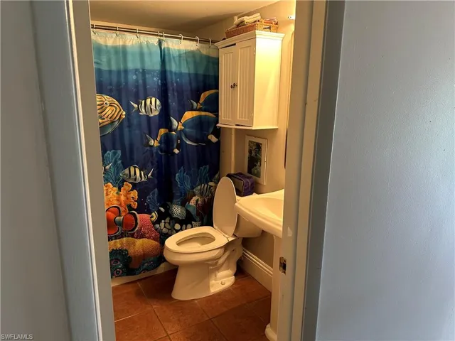 Bathroom with a shower with shower curtain, tile patterned floors, and toilet