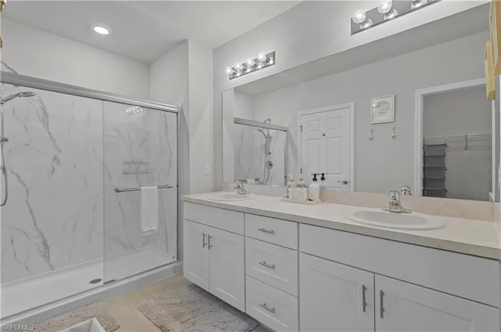 Full bath with a marble finish shower, double vanity, a walk in closet, tile patterned floors, and recessed lighting