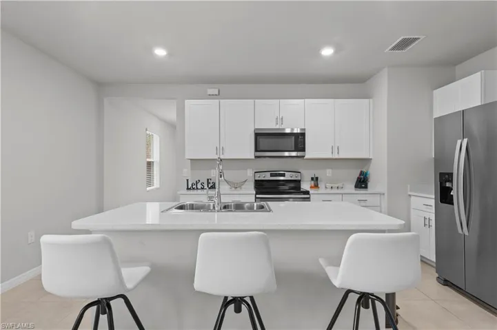 Kitchen with appliances with stainless steel finishes, a breakfast bar, light tile patterned floors, white cabinets, and recessed lighting