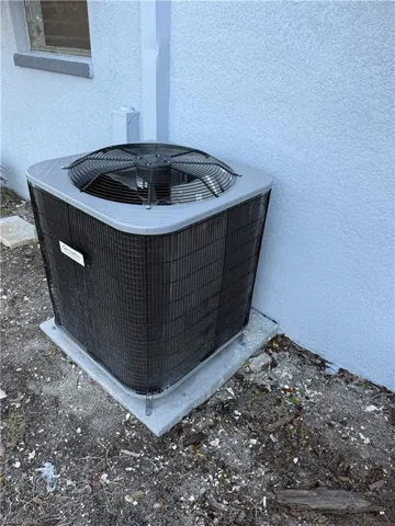 Exterior air conditioning unit on a concrete pad, positioned against a textured stucco wall