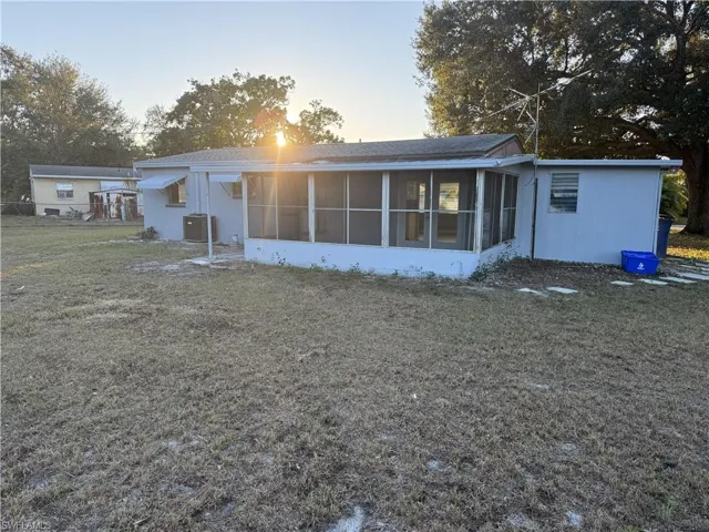 Rear exterior featuring an enclosed screened porch, a separate utility structure, and mature trees in the background