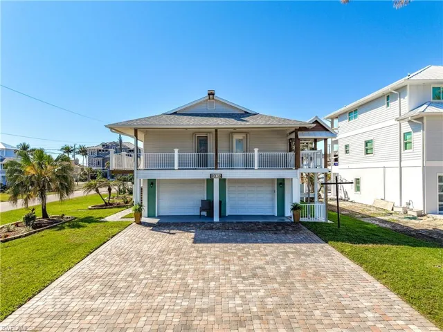 Coastal inspired home with a shingled roof, a front yard, decorative driveway, and an attached garage