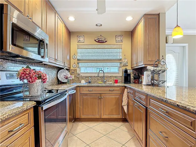Kitchen featuring light tile patterned floors, stainless steel appliances, a sink, tasteful backsplash, and brown cabinetry