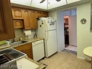 Kitchen with brown cabinetry, a ceiling fan, white appliances, decorative backsplash, and light tile patterned floors